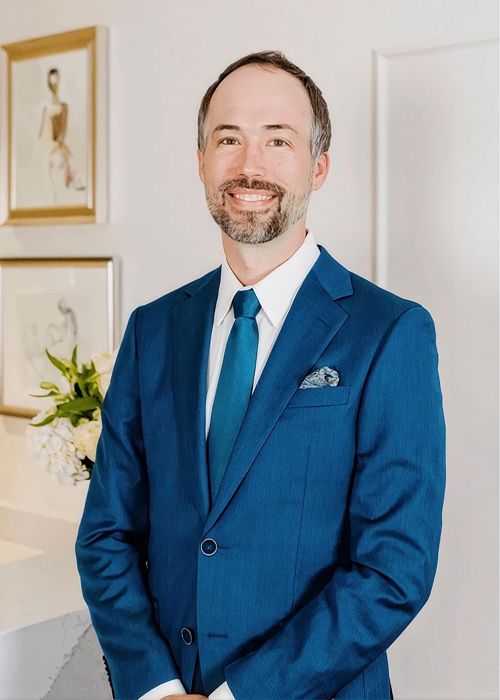 Smiling man in a blue suit standing indoors.