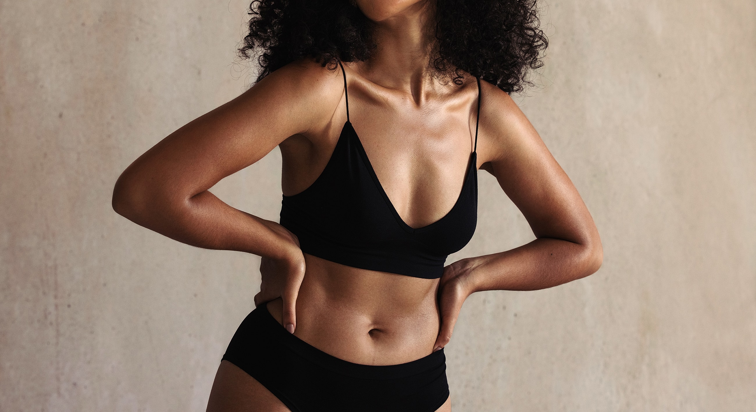 Model posing in black lingerie against textured background.